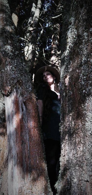 Michela standing between two ancient trees, wearing a hat