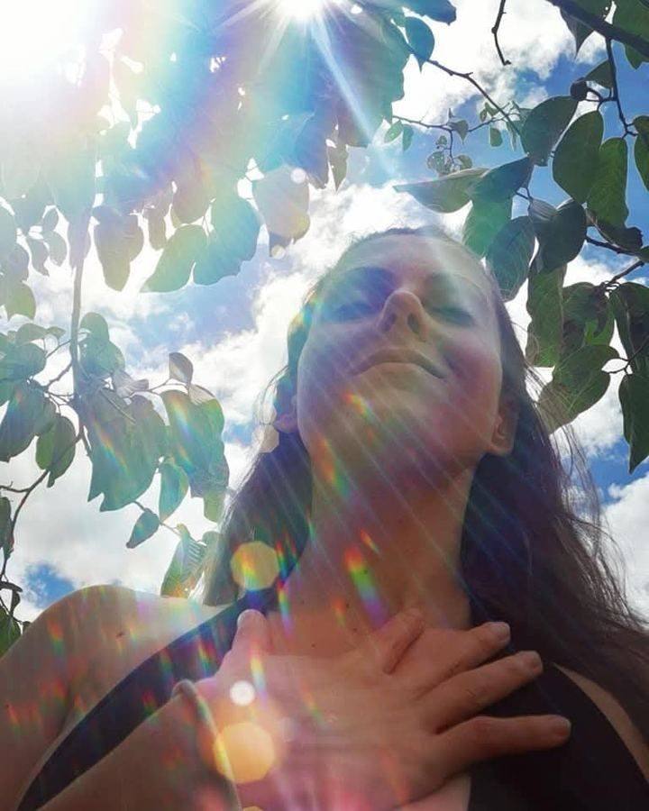Hand over heart, eyes closed, rainbow light through the leaves — Breathing & Grounding