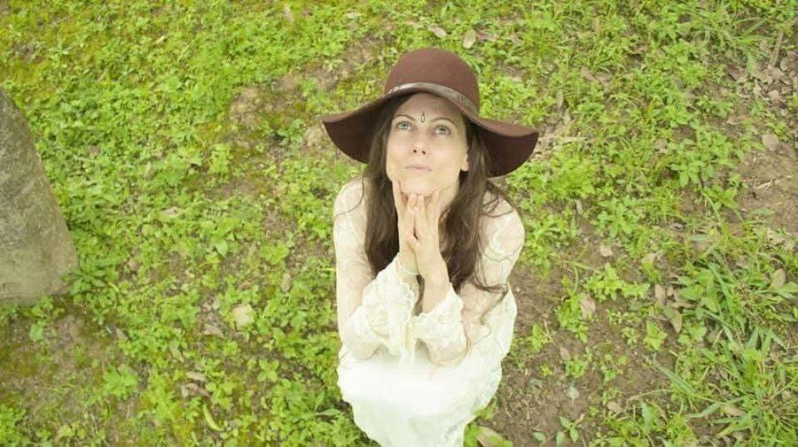 Michela en oración, sombrero y manos entrelazadas, en el campo — Oraciones e Invocación