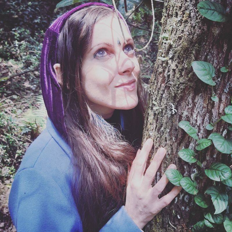 Michela close, touching the bark of a tree, dappled light on her face
