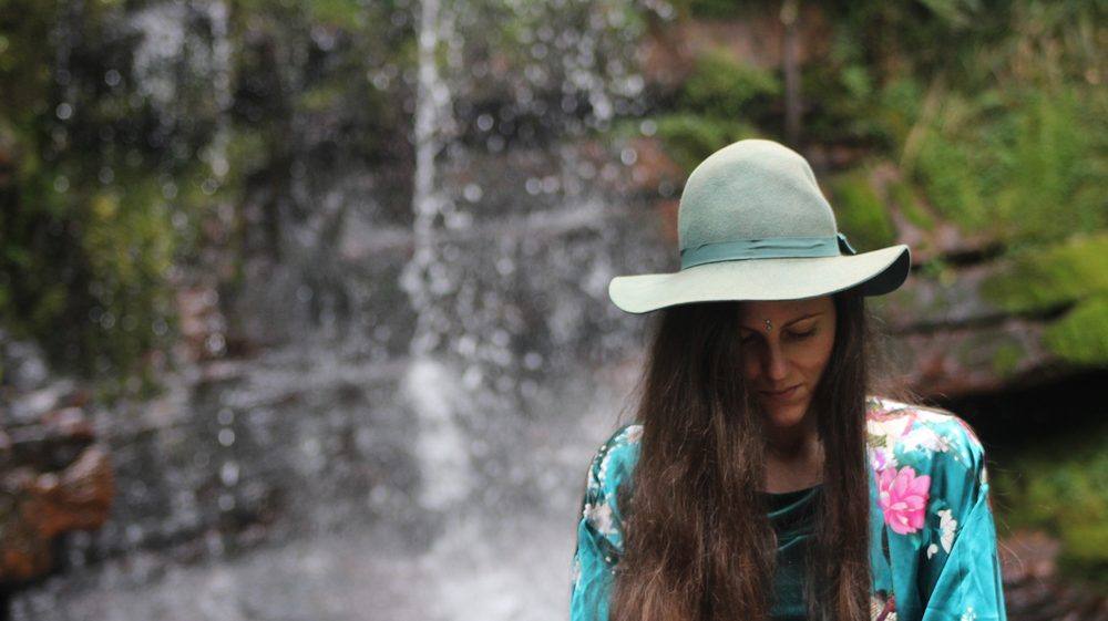 Michela beneath a waterfall, wearing a wide-brimmed hat