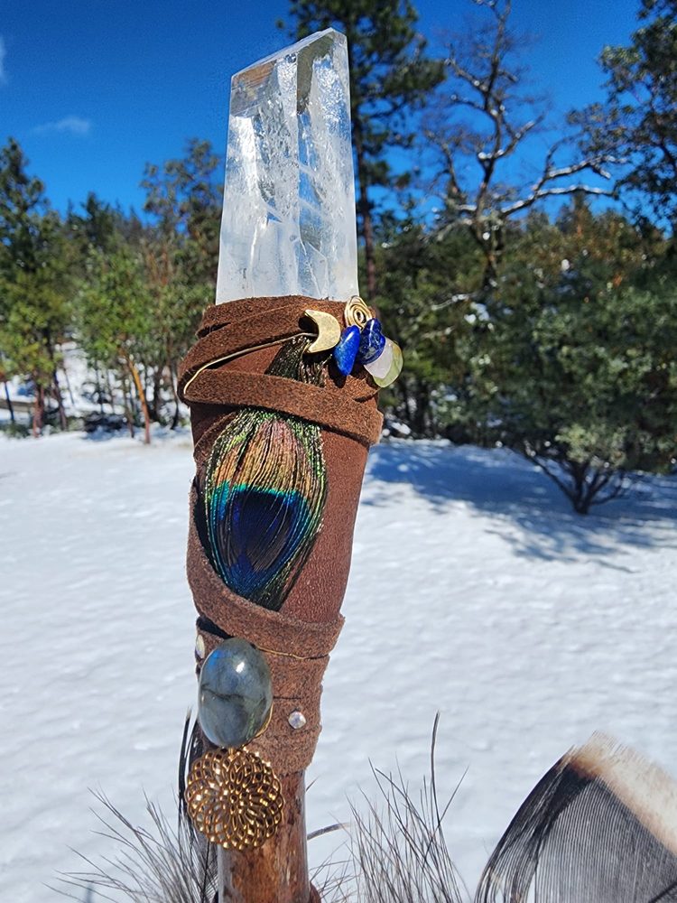 Sacred crystal wand with peacock feather in snow
